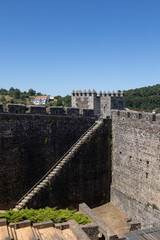 Sabugal Castle in Portugal features imposing stone walls and a historic stone staircase, showcasing its medieval architecture. The image captures the fortress under a clear blue sky