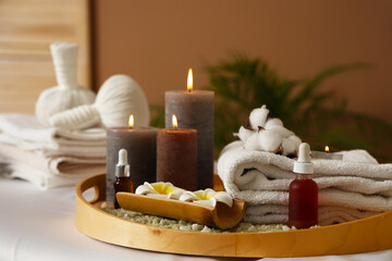 Burning candles with flowers and towels on couch in spa salon, closeup