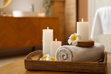 Burning candles with flowers and towel on table in spa salon, closeup