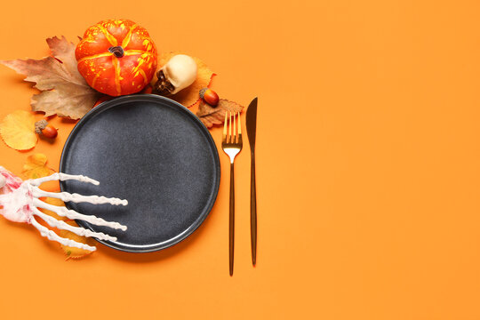 Halloween table setting with skeleton hand and autumn decor on orange background