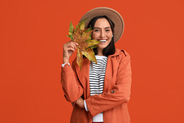 Beautiful young woman with autumn leaves on red background