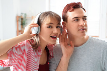 Young man with hearing aid and his girlfriend in headphones at home, closeup