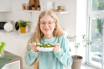 Young woman holding plate of tasty salad with feta cheese in kitchen