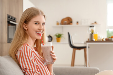 Young woman with healthy smoothie sitting on sofa at home