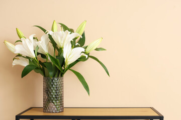 Table with vase of lily flowers near beige wall in room, closeup