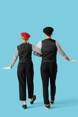 Couple of pantomimists on blue background, back view