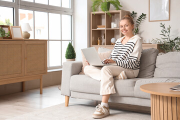 Young woman using modern laptop on sofa at home