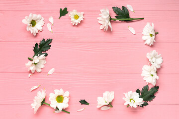 Frame made of beautiful chamomile flowers on pink wooden background