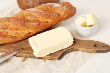 Wooden board with fresh butter and bread on light table