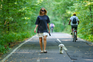 Girl walking the dog in the park forest. Rest concept. Woman walking with a dog on a leash in blue dress and with shoes.