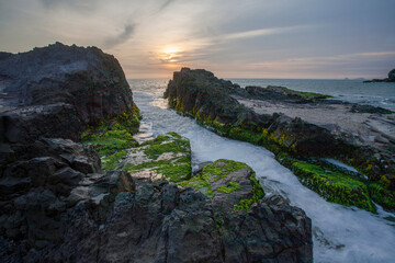 Moss-covered rocks with ocean waves and sunset sky