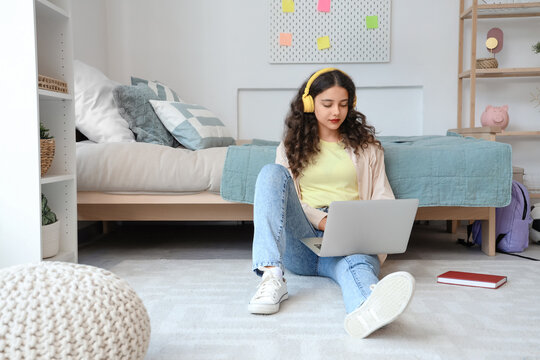 Teenage girl with headphones and laptop studying on floor in bedroom
