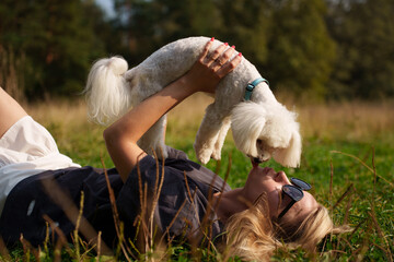 The beautiful woman lies on the grass and hug with her dog. The girl have a fun tome with the dog....