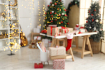 Beautiful gift boxes with packing materials and decorations on table near Christmas trees at home, blurred view