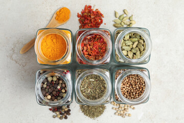 Different spices in glass jars on light grey table, top view