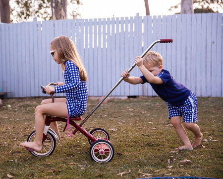 sister and brother riding a trike in a back yard