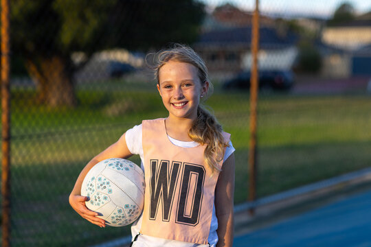 schoolgirl standing with netball under her arm and smiling at camera