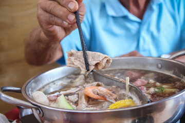 Old man Hand holding chopsticks with pork over shabu hot pot Thai food background