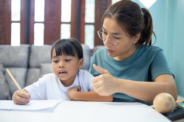 A young girl is sitting at a table with her mother, looking at a tablet.