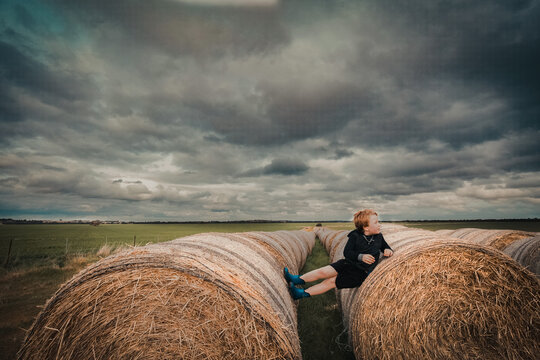 Child sitting on long row of round hay bales on cloudy day