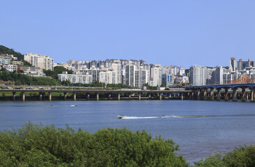 Naklejka premium Oksu-dong, Seongdong-gu, Seoul, South Korea - August 15, 2021: Summer view of water ski and motorboat on Han River against Gangbyeon Expressway and highrise apartments