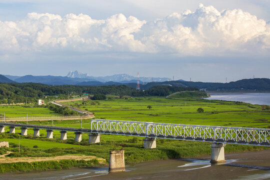 Imjingak Pavilion, Paju-si, Gyeonggi-do, South Korea - August 9, 2021: High angle view of an iron bridge on Imjingang River with rice field at Peace Nuri Park against Bukhansan Mt in the background