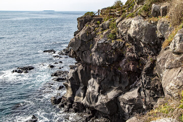 High angle view of cliffs with volcanic rocks and wood fence against sea horizon at Jeju-si,...