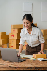 E-commerce Success: A young Asian woman entrepreneur beams with pride as she manages her thriving online business, surrounded by stacks of shipping boxes and a laptop. Her confident smile and focused 