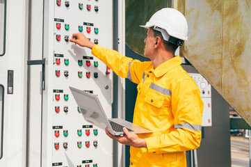 The electrician inspects a large-scale industrial electrical control system, focusing on the safety...