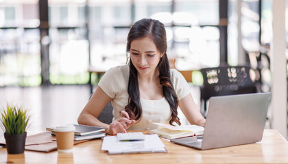 Asian young business woman working on laptop computer reading financial document report in office. Accountant entrepreneur manager businesswoman doing paperwork. Copy space