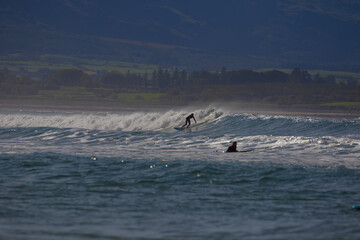 yellowish-white waves with surfers against a blue sky. 