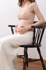椅子に座って妊娠したお腹に手を添える若い女性