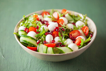 Vegetable salad with cheese and pomegranate grains on a green background