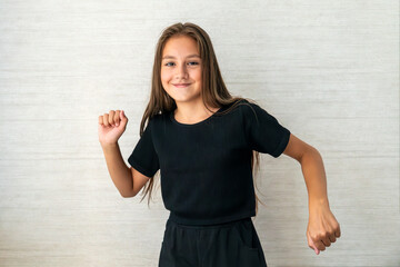 Portrait of attractive, happy girl with hair gathered in a bun. Wearing black t-shirt . Lifts her arms and dance with closed eyes. Stand on white background