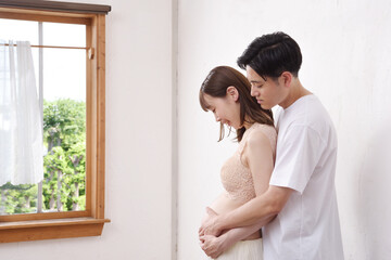 窓辺で寄り添う若い妊婦と夫