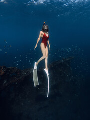 Woman free diver dives in blue ocean on wreck ship in Bali.