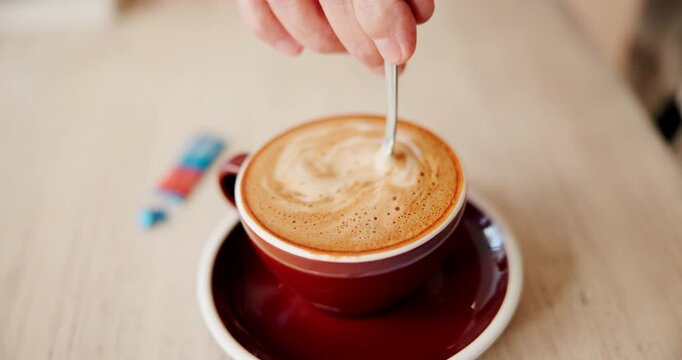 Person, stir and hand with coffee on table for morning, sweetener and preparation of beverage. Mixing, sugar and top view with mug by customer for restaurant, cappuccino and caffeine in warm drink