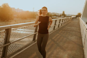 Determined runner jogs along a sunlit bridge during the golden hour, blending fitness and serenity in an urban landscape