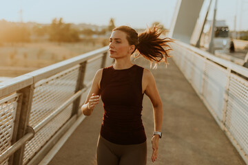 Determined runner jogs along a sunlit bridge during the golden hour, blending fitness and serenity in an urban landscape