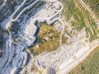 Stone quarry in the forest. Flying over the summer mixed forest during sunset. The surroundings of Yekaterinburg. Ural, Russia, Aerial View
