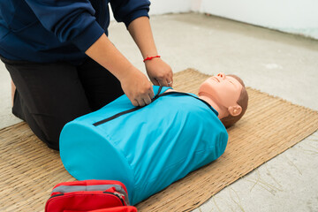 A woman studies at a gas station with an adult CPR dummy on the floor. She practices situation...