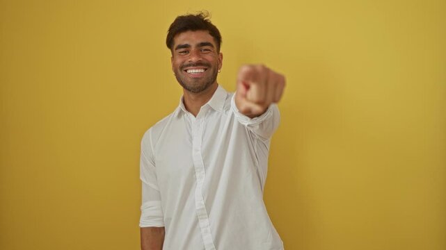 Young man with a smile pointing confidently at the camera against an isolated yellow background.