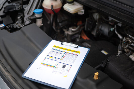 A multi-point car maintenance and inspection checklist paper on clipboard, that placed at car front hood. It using as standard guideline for car service job. Close-up and selective focus.