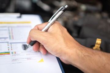 Close-up at a mechanic foreman's hand is checking on multi-point car service guideline checklist form, to verify the car service quality. Expertise working action scene, selective focus.