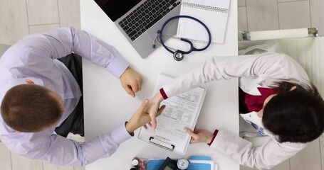 Doctor shaking hands and concluding health insurance contract with a patient at consultation in a hospital, top view