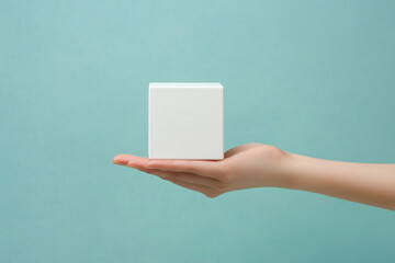 Minimalism concept image with a person hand holding a minimalist plain white cube shape object isolate on an empty blue background