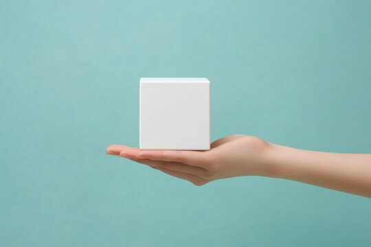 Minimalism concept image with a person hand holding a minimalist plain white cube shape object isolate on an empty blue background