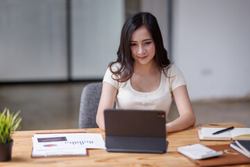 Businesswomen or Asian Accountants using calculator and a tablet laptop computer to analyze business report graphs and finance charts at the workplace, financial and investment concept.
