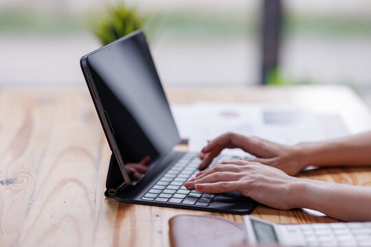 Businesswomen or Asian Accountants using calculator and a tablet laptop computer to analyze business report graphs and finance charts at the workplace, financial and investment concept.
