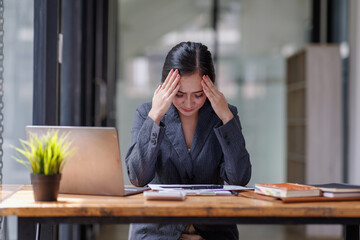 Portrait of tired young business Asian woman headache while working  with documents tax laptop computer in office. Sad, unhappy, Worried, Depression, or employee life stress concept